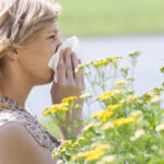 Woman blowing nose into tissue in front of flowers Image