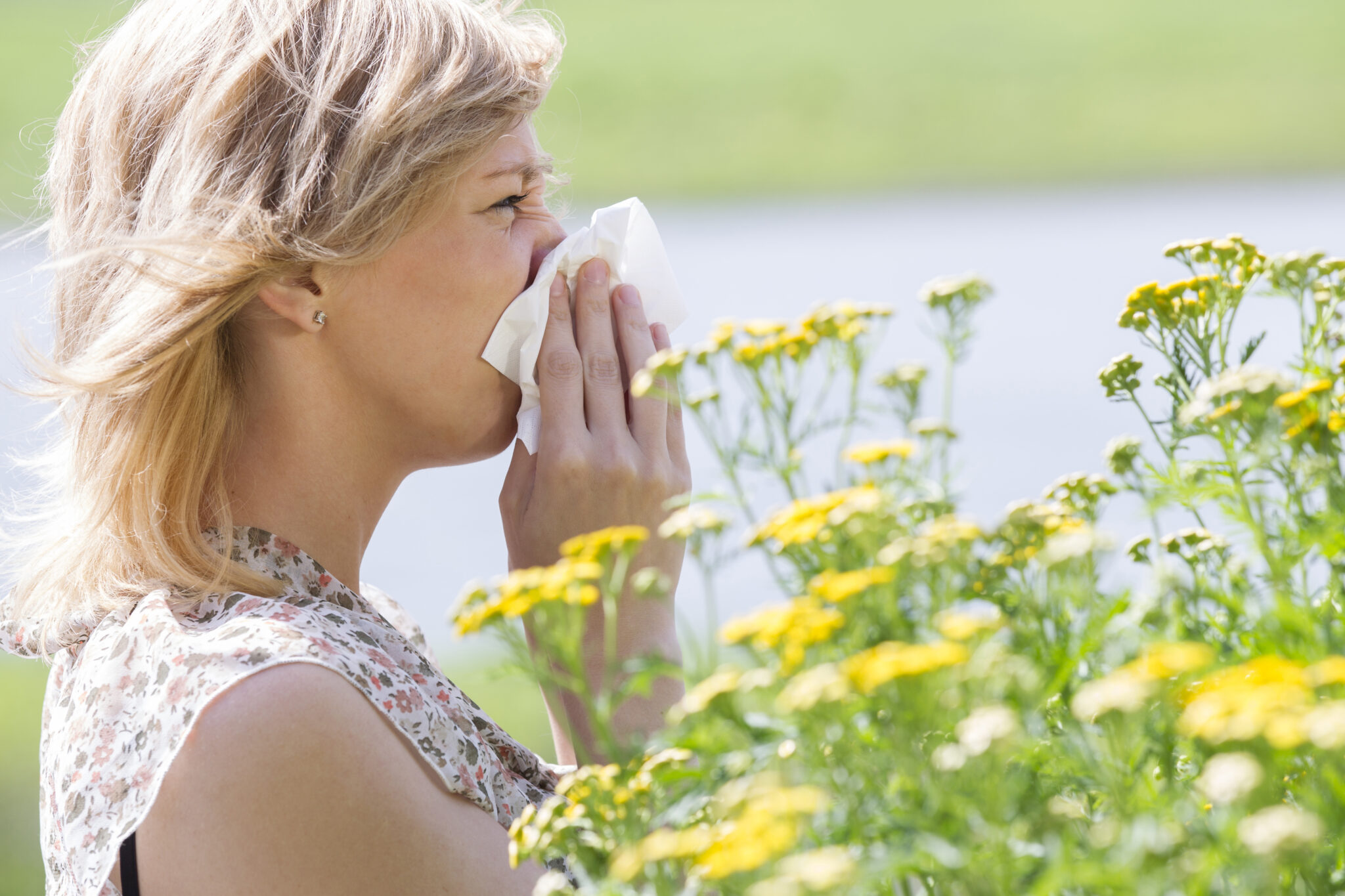 Woman blowing nose into tissue in front of flowers Image